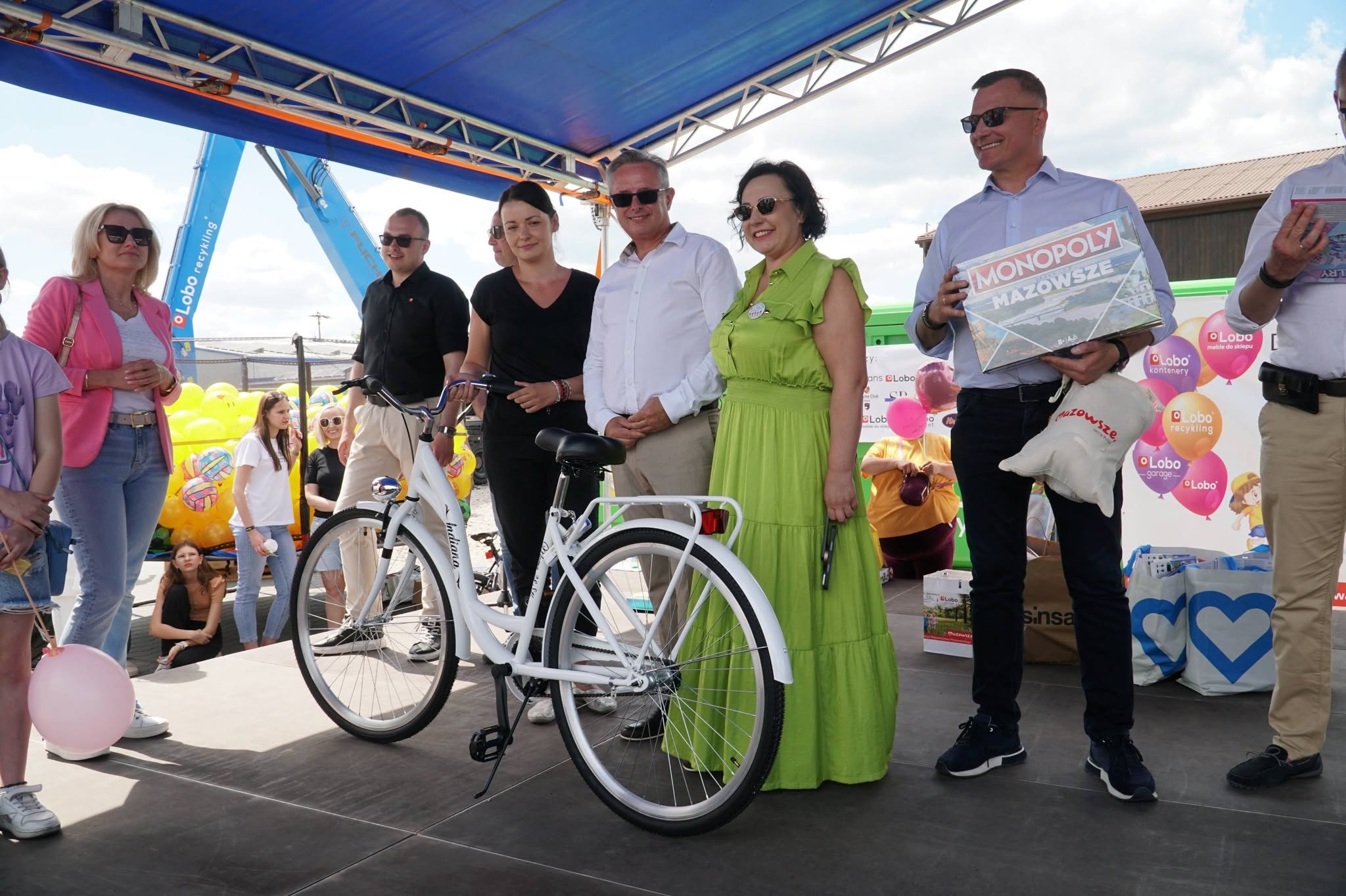 Zdjęcie przedstawia grupę ludzi na scenie, kt&oacute;ra przekazuje rower. 