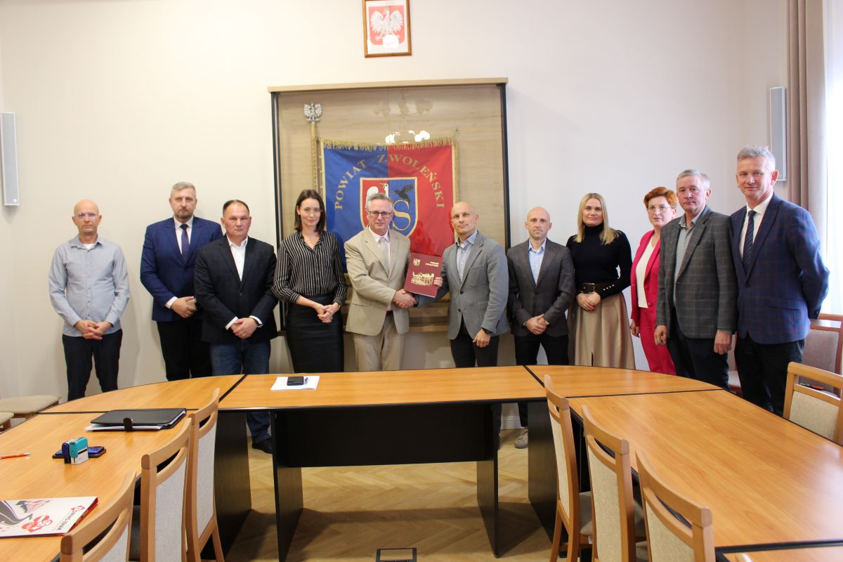 Zdjęcie przedstawia grupę osób stojących na sali narad w Starostwie Powiatowym w Zwoleniu