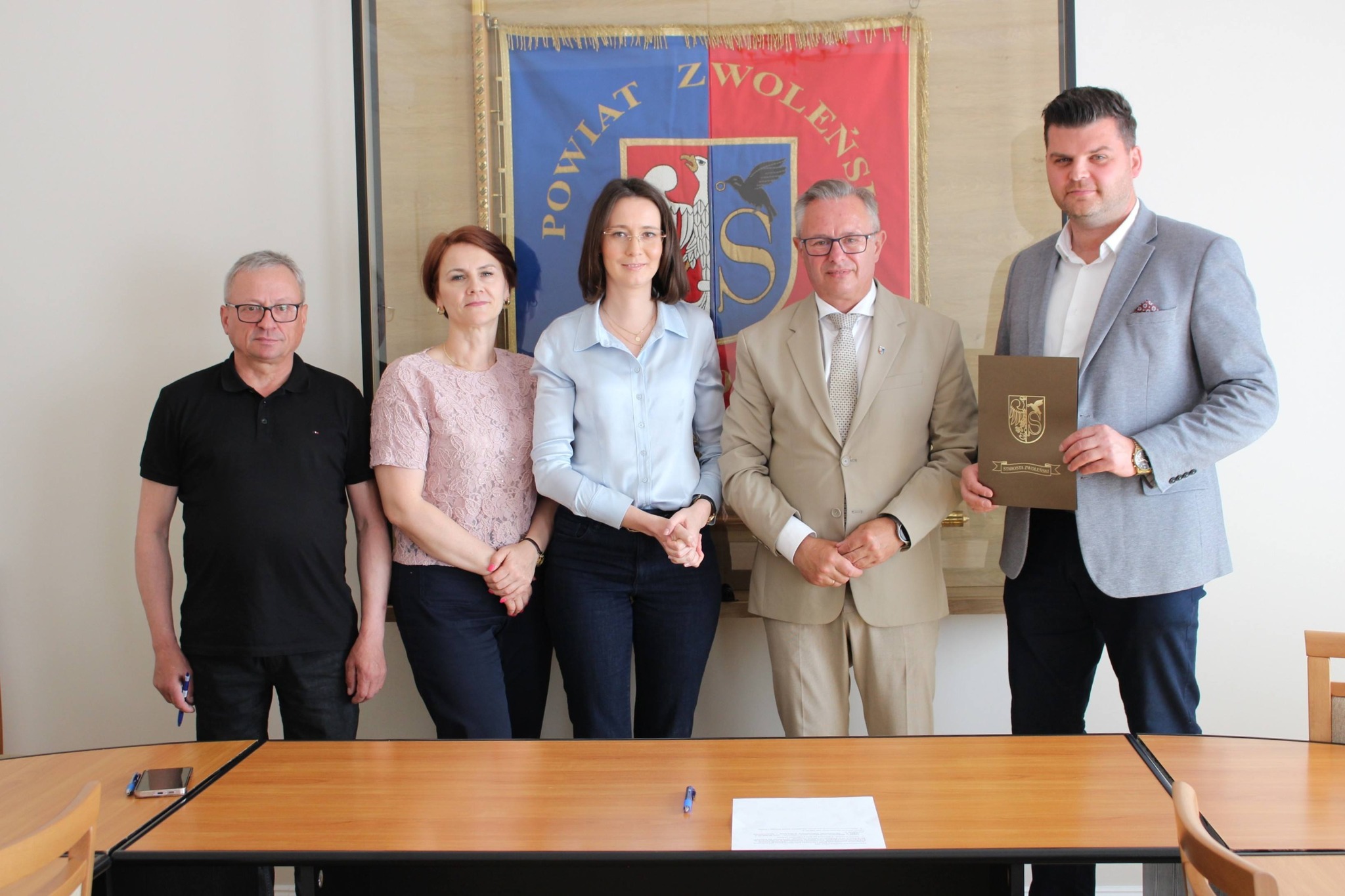 Podpisanie umowy Zdjęcie przedstawia grupę osób stojących na tle sztandaru powiatu zwoleńskiego.