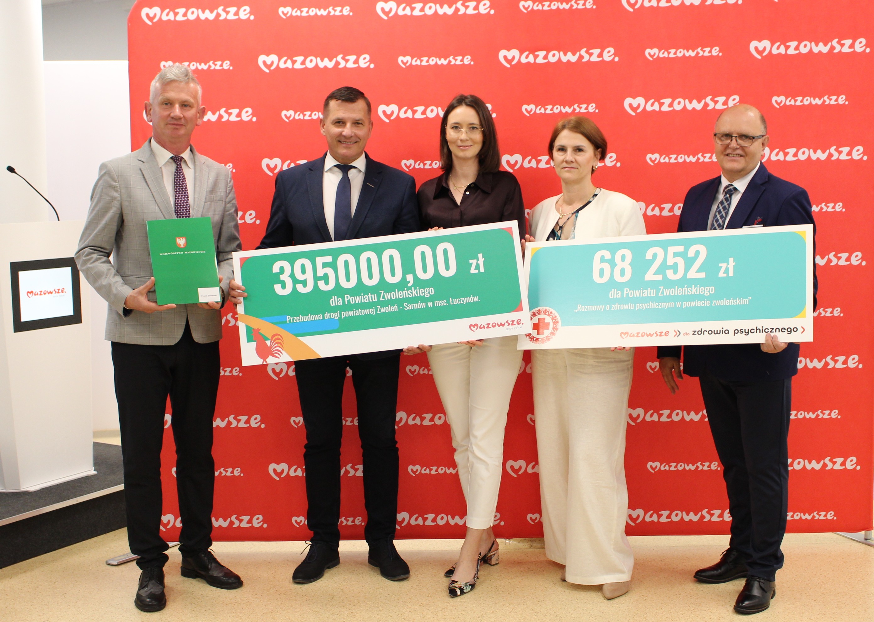 Zdjęcie przedstawia grupę os&oacute;b z czekami na tle ścianki.
