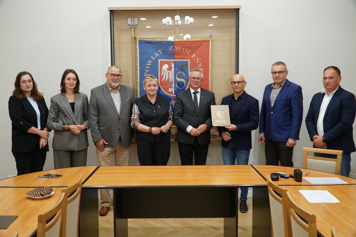 Zdjęcie przedstawia grupę os&oacute;b stojących na tle sztandaru Powiatu Zwoleńskiego po podpisaniu umowy.
